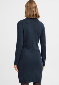 Marinblå stickad kl�änning med långa ärmar, rundad halsringning och ribbad nederkant. Tygets textur ser mjuk och något strukturerad ut.