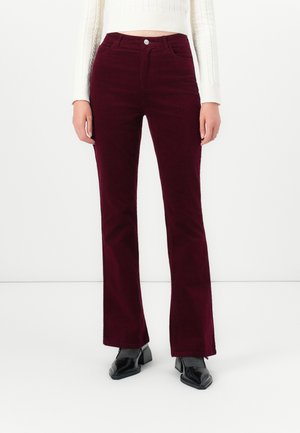 Woman wearing high-waisted, dark burgundy corduroy pants paired with black heeled shoes and a white cropped sweater.