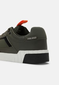 Green sneaker featuring a textured upper, black accents, white midsole, and an orange pull tab at the heel with "BLEND" branding.