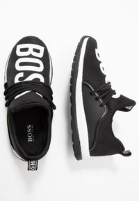 Zapatillas BOSS de color negro y blanco con parte superior de tejido, suelas interiores gruesas blancas, suelas exteriores negras y cordones negros, mostradas desde vistas superior y lateral.