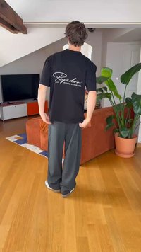 Black cotton t-shirt with white text "Pegador" and "ALL RIGHTS RESERVED" on back; loose fit, worn with gray wide-leg pants.
