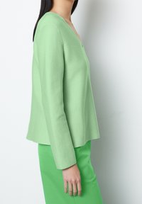 Light green pullover sweater with a V-neck, ribbed texture, long sleeves, and a relaxed fit, paired with a matching green skirt.