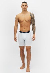 Vita boxerkalsonger tillverkade av mjukt tyg med en marinblå midja, med en tajt passform och täckning upp till mitten av låret. Inga mönster eller dekorationer.