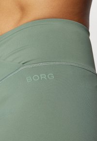 Top attivo verde realizzato in un tessuto liscio e elastico con una leggera lucentezza. Logo "BORG" in rilievo, cuciture piatte lungo i bordi.