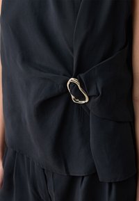 Top blu navy realizzato in morbido tessuto, caratterizzato da un design annodato con un accento argento di forma irregolare in vita. Texture liscia.