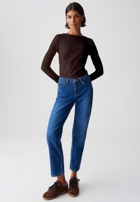 Brown ribbed long-sleeve top paired with blue straight-leg jeans and brown suede sneakers. Clean lines and casual fit.