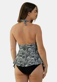 Haut de maillot de bain noir et blanc floral avec un design peplum, lien ajustable au cou, associé à un bas de bikini noir uni.