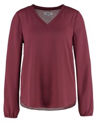 Blouse bordeaux à manches longues avec un col en V, fabriquée en tissu lisse, présentant des poignets froncés et un ourlet courbé avec une doublure intérieure texturée.