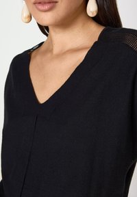 Maglione nero a maglia con scollo a V e dettagli testurizzati sulle spalle. Il tessuto appare morbido e leggermente aderente.