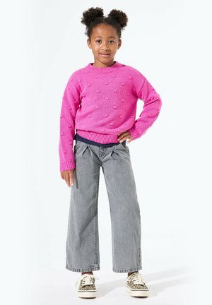 Rosa gestrickter Pullover mit strukturierten Punkten, kombiniert mit hoch taillierten grauen weit geschnittenen Jeans und gemusterten Turnschuhen. Im entspannten Stil gestaltet.