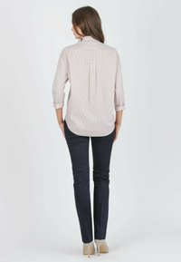 Helles, gestreiftes Hemd mit hochgerollten Ärmeln, Rückenteil mit Falten, kombiniert mit eng anliegenden navyblauen Hosen und beigen Absätzen. Schlichtes, maßgeschneidertes Design.