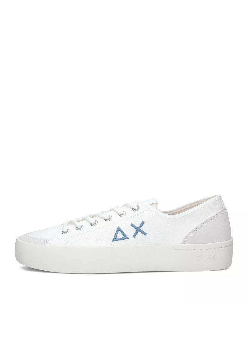 Zapatilla blanca de caña baja con triángulos azules y símbolos X en el lateral, cordones blancos y suela de goma gruesa sobre un fondo blanco.