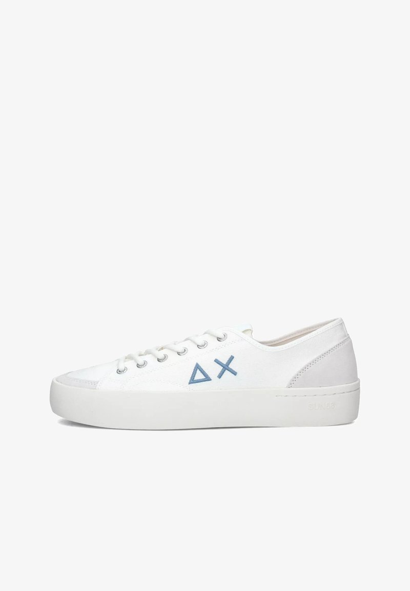 Zapatilla blanca de caña baja con triángulos azules y símbolos X en el lateral, cordones blancos y suela de goma gruesa sobre un fondo blanco.