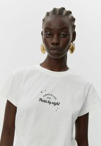 Bela bombažna majica s kratkimi rokavi, na kateri je črn napis "Vedno zaljubljen v Pariz ponoči" s pljuski majhnih zvezd.