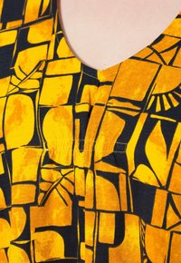 Tessuto giallo e nero a fantasia con scollo a V, caratterizzato da forme geometriche e design astratti, superficie texturizzata con leggera lucentezza.
