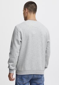 Sudadera gris, diseño de cuello redondo, mangas largas, con puños y dobladillo de canalé. Material de algodón suave con una textura lisa. Vista trasera simple y sin adornos.