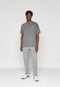 Γκρι βαμβακερό t-shirt με το "City" κεντημένο σε πορτοκαλί, συνδυασμένο με ανοιχτό γκρι φούτερ παντελόνι και άσπρα αθλητικά παπούτσια με μαύρες λεπτομέρειες.