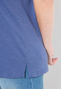 Niebieska bawełniana koszulka z krótkim rękawem, z bocznym rozcięciem u dołu. Noszona na jasnoniebieskich dżinsach, ukazujących teksturowany materiał. Prosty fason.