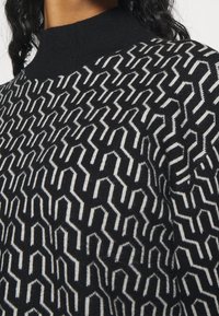 Black and white patterned sweater featuring a high neck design, with a zigzag texture and geometric shapes throughout.