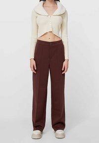 Crème cropped cardigan met een zachte kraag en knoopsluiting, gecombineerd met hoge, wijde bruine broeken. Glad materiaal en een op maat gemaakte pasvorm.