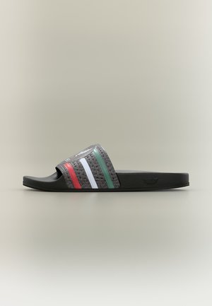 Sandale slide noire unique avec une sangle texturée comportant des rayures rouges, blanches et vertes, et un logo en relief sur le côté de la semelle.