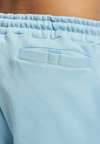 Pantaloni de trening bleu deschis, cu un talie elastică, având o mică buzunar pe spate cu clapetă și un material texturat, moale.