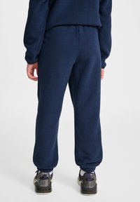 Marina stickade joggers med elastisk midja, manschetter vid anklarna och en mjuk textur. Bärs med grå och lila sneakers.