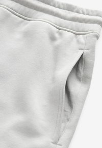 Svijetlosive trenirke s mekanom teksturom, elastičnim pojasom i dizajnom sa bočnim džepovima. Materijal izgleda glatko s minimalnim detaljima šavova.