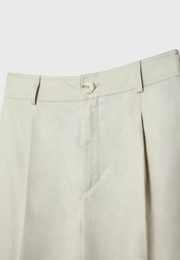 Světlé béžové kalhoty s vysokým pasem, s poutky na opasek, předním zapínáním na knoflík a hladkým, jemným textilním povrchem.