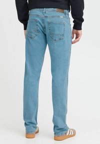 Jeans de color azul claro con corte recto, que presentan dos bolsillos traseros con un diseño sutil en ángulo y una etiqueta de cuero marrón en la cinturilla.