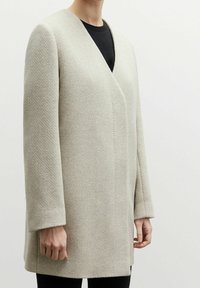 Ljusgrått omslagsjacka i en texturerad stoff, med en v-ringning och långa ärmar. Designen är minimalistisk och rak skuren.