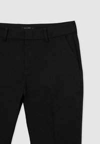 Pantalons noirs ajustés avec une conception à l'avant plat, des poches latérales et des passants de ceinture. La texture du tissu semble lisse, adaptée à une tenue formelle ou décontractée.