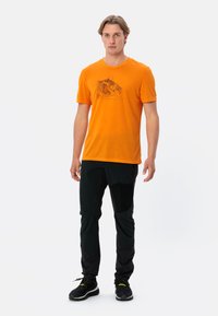 Oranje katoenen T-shirt met een grafische print van een berglandschap aan de voorkant. Draagt het met zwarte multifunctionele broek en zwarte schoenen.