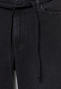 Gros plan sur un pantalon en denim noir avec une poche avant visible, un passant de ceinture et un cordon noué à la taille.