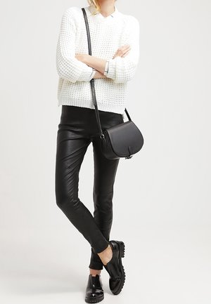 Weißer gestrickter Pullover, schwarze Kunstlederhose, schwarze Umhängetasche und schwarze Schuhe mit strukturierten Sohlen. Lässiges Outfit mit kontrastierenden Stilen.