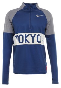 Long-sleeve blue and gray sports top with a half-zip, white horizontal stripe reading "TOKYO," and white Nike logo on the chest.