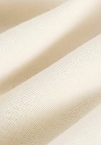 Weiches, cremefarbenes Strickgewebe mit glatter Textur und dezentem Webmuster, dargestellt in sanften Falten.