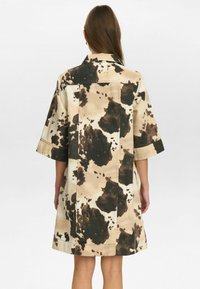 Korte mouwen beige jasje met een bruin en zwart abstract patroon, voorzien van een klassieke kraag en een rechte snit. Gestructureerde stof met zichtbare stiksels.