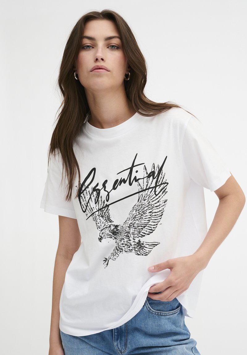 Hvid kortærmet t-shirt med et sort ørnegraphic og "Essential"-tekst. Lavet af et let stof med en afslappet pasform.