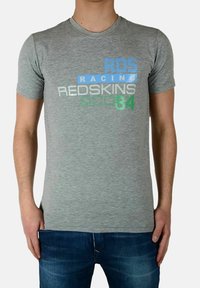 T-shirt grigio a maniche corte con testo blu, verde e argento che riporta "RDS", "RACING" e "REDSKINS" in diversi caratteri e dimensioni. Tessuto morbido.