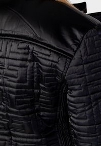 Schwarze gesteppte Jacke mit einer glatten, glänzenden Textur und einem geometrischen Muster. Sie verfügt über einen strukturierten Kragen und gerippte Details.