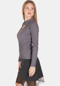 Top grigio a maniche lunghe con righe, caratterizzato da un collo alto e un taglio frontale, abbinato a una gonna nera con pizzo lungo l'orlo.