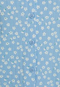 Jasnoniebieska prążkowana tkanina z małymi białymi kwiatami i zielonymi akcentami. Ma niebieskie guziki wzdłuż środka do zapięcia.