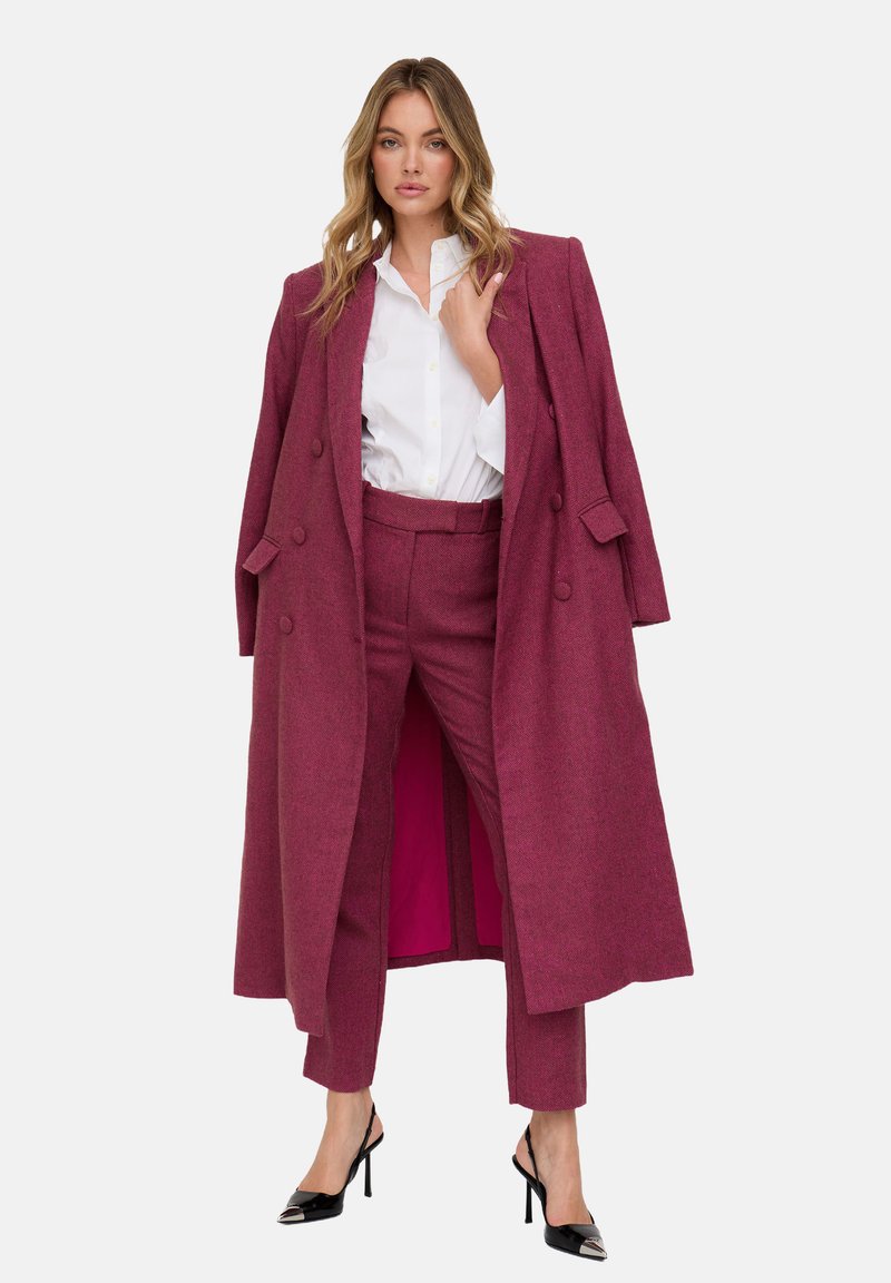 Mantel aus einer Wollmischung in Kastanienbraun mit doppelreihigem Design, kombiniert mit passenden, maßgeschneiderten Hosen und einem weißen Hemd mit Knöpfen. Schwarze High Heels vervollständigen den Look.