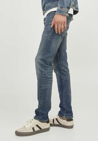 Jeans de color azul oscuro con un diseño ajustado, que cuentan con un estilo clásico de cinco bolsillos. Llevados con zapatillas de color claro con acentos en negro.