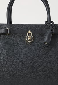 Sort læder håndtaske med pebble-textur, dobbelte top-håndtag, hardware i guldfinish og en logo-lås charm. Kompakt og struktureret design.