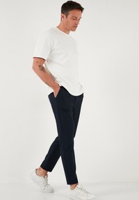 Witte kortebloemige t-shirt, gecombineerd met marineblauwe slim-fit broek en witte sneakers. De outfit heeft een minimalistisch ontwerp en een gladde textuur.