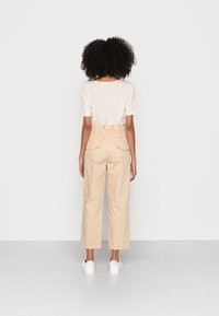 Pantaloni beige a gamba larga con vita elastica, dotati di due tasche posteriori. Abbinati a una maglietta a righe di colore chiaro e sneakers bianche.