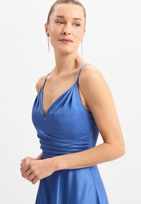 Koninginblauwe satijnen jurk met een V-hals, geplooide lijf en dunne bandjes. De gladde textuur en de vloeiende rok creëren een elegante silhouet.