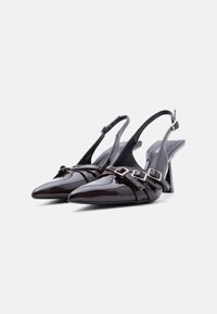 Paire d'escarpins slingbacks noirs brillants à bout pointu, avec trois brides et boucles argentées sur fond blanc.